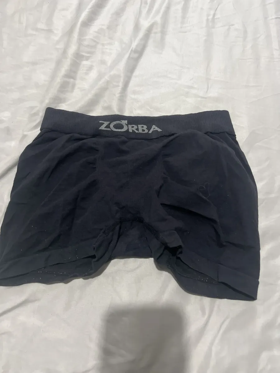 Foto de cliente mostrando cueca Zorba preta aberta sobre lençol claro